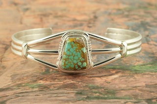 Genuine Number 8 Turquoise set in Sterling Silver. Stunning heavy gauge Sterling Silver Bracelet with a Beautiful Turquoise Stone. The Number 8 mine is located in Eureka County Nevada. Since 1976 there has been no Number 8 Turquoise mined. There is however, an existing stock pile that Mr. Dowell Ward, the last owner of the Number 8 mine, had stocked away for later sorting. The Turquoise is a collector's item--because once the reserve is gone there will be no more material released onto the market. The Gold Mining Company owns the claim to the Number 8 mine and it has been swallowed up by the gold mining operations. This is some of the last Number 8 Turquoise to be had and will be a great addition to your collection. Created by Navajo Artist Arkie Nelson. Signed by the artist.
