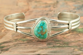 Genuine High Grade Kingman Web Turquoise set in Sterling Silver Bracelet. Created by Navajo Artist Milton Lee. Signed by the artist. The Mineral Park Mine, in the Cerbat Mountains 14 miles northwest of Kingman, was first mined by Indians centuries before white man came to the area. It is one of the three sites of prehistoric mining localities in the state of Arizona. Mineral Park was the most extensively worked area by the Indians of the three. S.A. �Chuck� Colbaugh found a cache of stone hammers uncovered in ancient trenches and tunnels, when he had the turquoise mining concession in May of 1962. Ithaca Peak and Turquoise Mine (formally called Aztec Mountain or Aztec Peak) are the most famous of the peaks in the area containing turquoise.